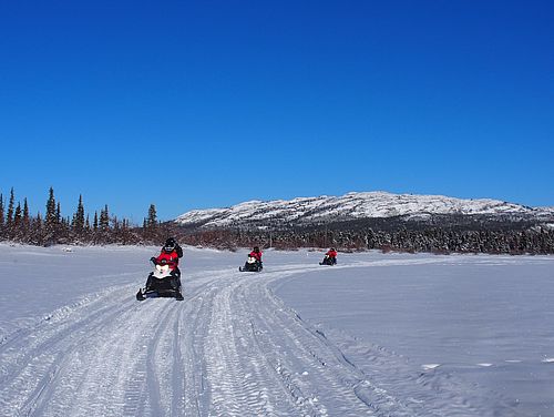 Gruppe von Snowmobilen unterwegs im verschneiten Yukon