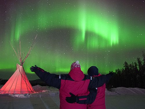 Zwei Reisende beobachten die grünen Nordlichter über dem Yukon Kanadas