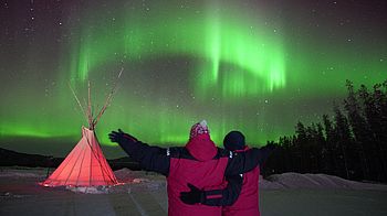 Zwei Reisende beobachten die grünen Nordlichter über dem Yukon Kanadas