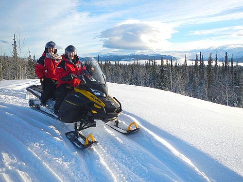 2 Personen auf einem Snowmobil vor einer Winterlandschaft im Yukon Kanadas