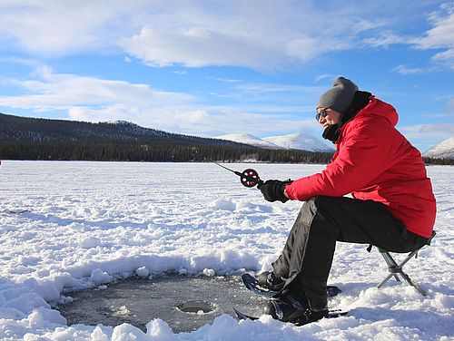 Person sitzt an einem Eisloch beim Eisangeln auf einem gefrorenen See