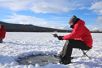 Person sitzt an einem Eisloch beim Eisangeln auf einem gefrorenen See